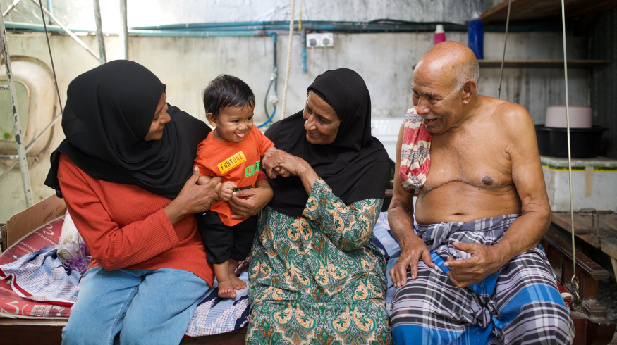 A family of four, mom, son, grandma and grandpa smiles at the son.