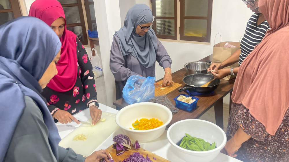 A group of lady cuts up ingredients to make food.