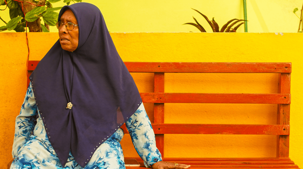 An elderly lady sitting on a bench stares to her left.